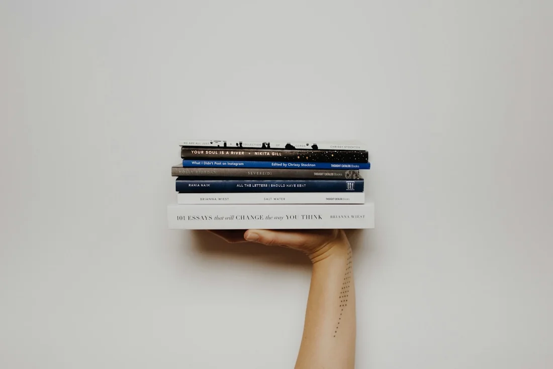 A hand holding a stack of books against a plain wall